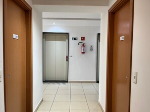 Ein Flur mit zwei Holztüren, einem Aufzug, einem Feuerlöscher und einem Schild, das den Weg zum Aufzug weist.