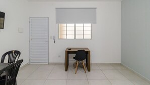 Una habitación con puerta cerrada, un escritorio con silla, una ventana con persianas y piso de baldosas.