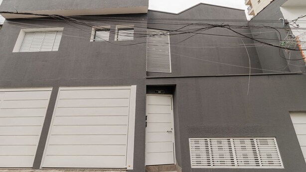 Un edificio moderno con dos puertas de garaje, una entrada pequeña y un ventanal con persianas.