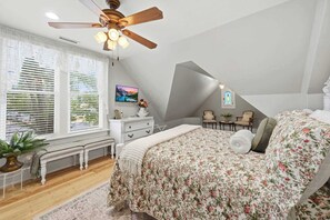 A bedroom with a bed, a ceiling fan, a TV, a window with blinds, a bench, a dresser, and a small table with a plant. - The Ultimate Historic Vibe: Queen Anne Victorian Meets Modern Indie Style Just Steps from The Courthouse Square (Prescott)