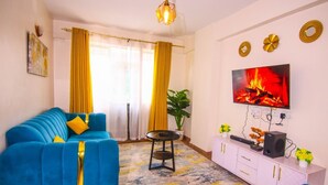 Una sala de estar con un sofá azul, un televisor montado en la pared, una mesita y un aparador con una planta encima.