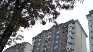 Un edificio residencial de varios pisos con balcones, una cerca y árboles.