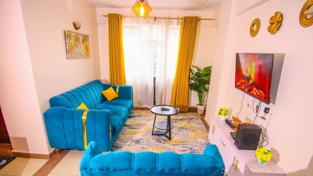 Una sala de estar con un sofá azul, una pequeña mesa redonda, un televisor y una planta.