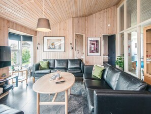 A modern living room with a wooden ceiling, black leather sofas, a round wooden coffee table, and framed artwork on the walls. - 5 Star Holiday Home in Juelsminde (Horsens)