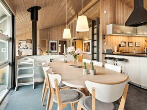 Une cuisine moderne avec un plafond en bois, des luminaires suspendus, un coin repas avec une table ronde et des chaises, et un bar avec des tabourets.
