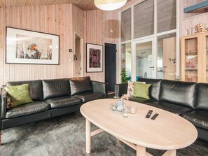 A modern living room with a black leather sofa, a wooden coffee table, and framed artwork on the walls. - 5 Star Holiday Home in Juelsminde (Horsens)