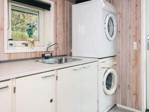 A compact kitchen with a sink, a window with a view of greenery, and a built-in washing machine. - 5 Star Holiday Home in Juelsminde (Horsens)
