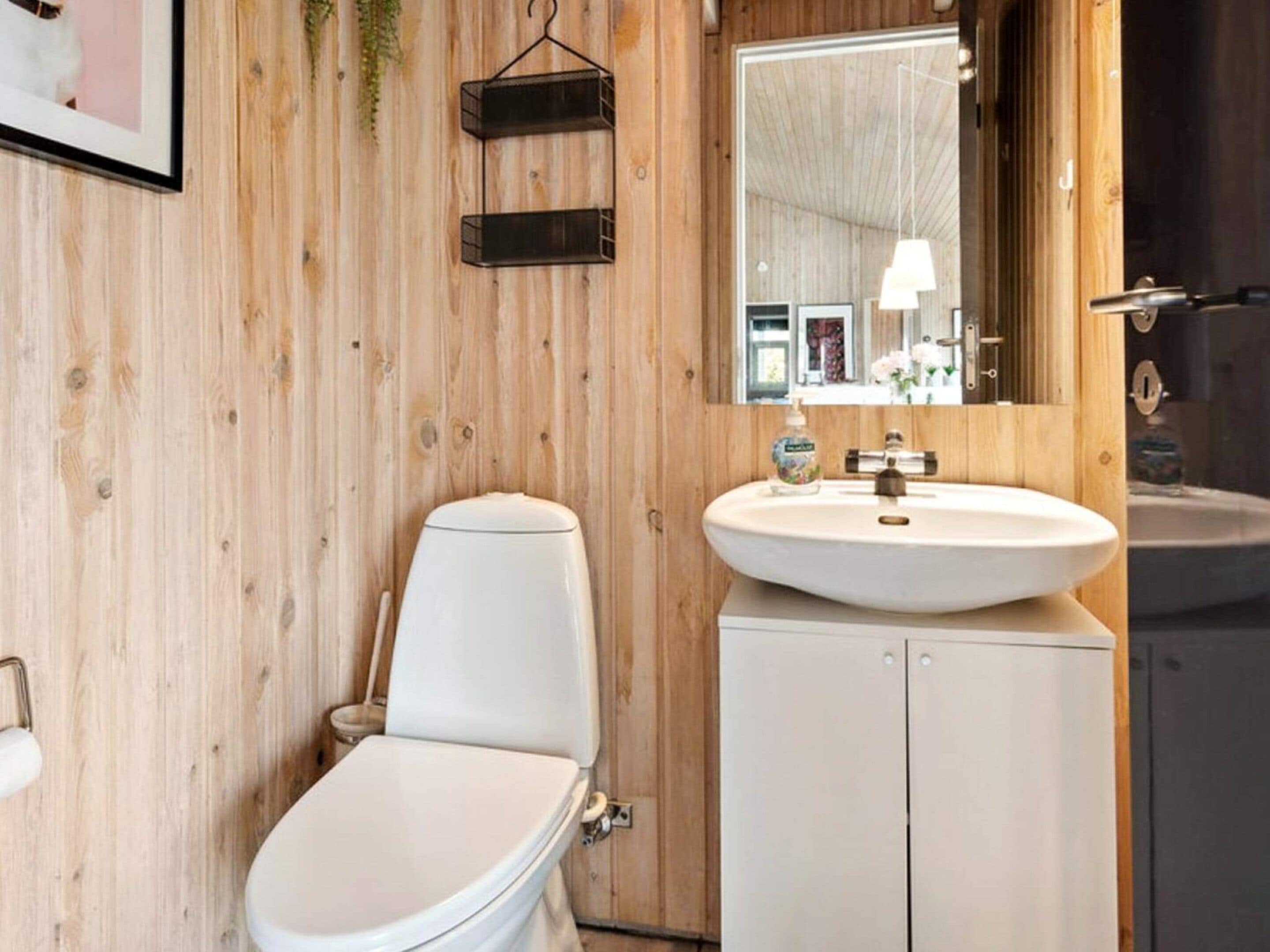 Un baño con inodoro blanco, lavamanos y espejo.