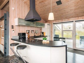 A modern kitchen with a central island, bar stools, a coffee machine, and a large window. - 5 Star Holiday Home in Juelsminde (Horsens)