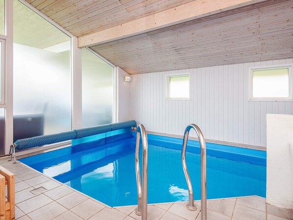An indoor swimming pool with a wooden ceiling, clear glass walls, and a tiled floor. - 5 Star Holiday Home in Juelsminde (Horsens)