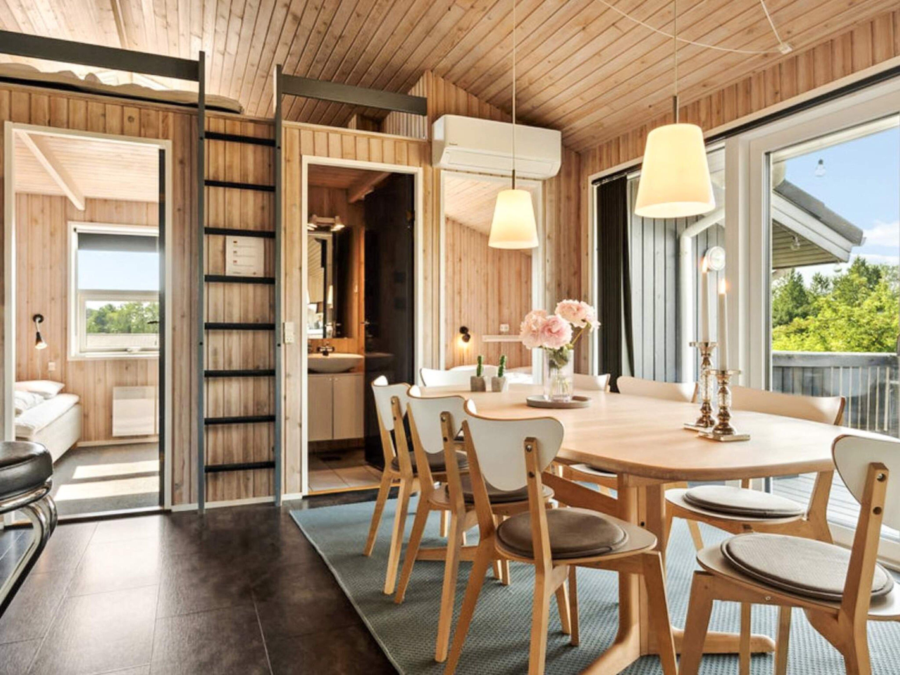 A modern interior with a wooden ceiling, a dining area with a round table and chairs, and a view through a large window.
