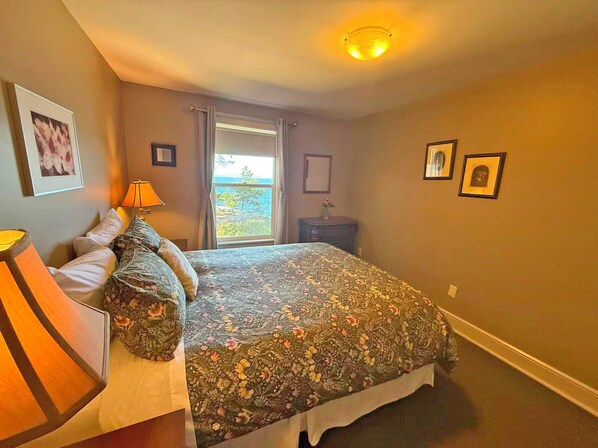 A bedroom with a bed, a nightstand, a lamp, a window with a view, and a ceiling light.