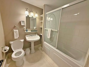 Une salle de bain équipée de toilettes, d’un lavabo, d’un miroir et d’une douche à parois en verre.
