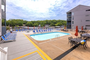A pool area with blue lounge chairs and tables, a pool, and a view of a forested area. - H Lakefront Property, Remodeled, Boat Slip, Patio Views, Pool, Ideal Location! (Osage Beach)