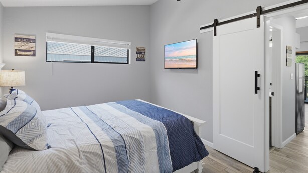 A bedroom with a bed, a ceiling fan, a window with blinds, a wall-mounted TV, and a door. - H Lakefront Property, Remodeled, Boat Slip, Patio Views, Pool, Ideal Location! (Osage Beach)