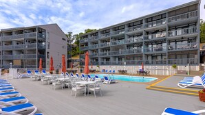 A poolside area with lounge chairs and umbrellas, a pool, and a multi-story building with balconies. - H Lakefront Property, Remodeled, Boat Slip, Patio Views, Pool, Ideal Location! (Osage Beach)