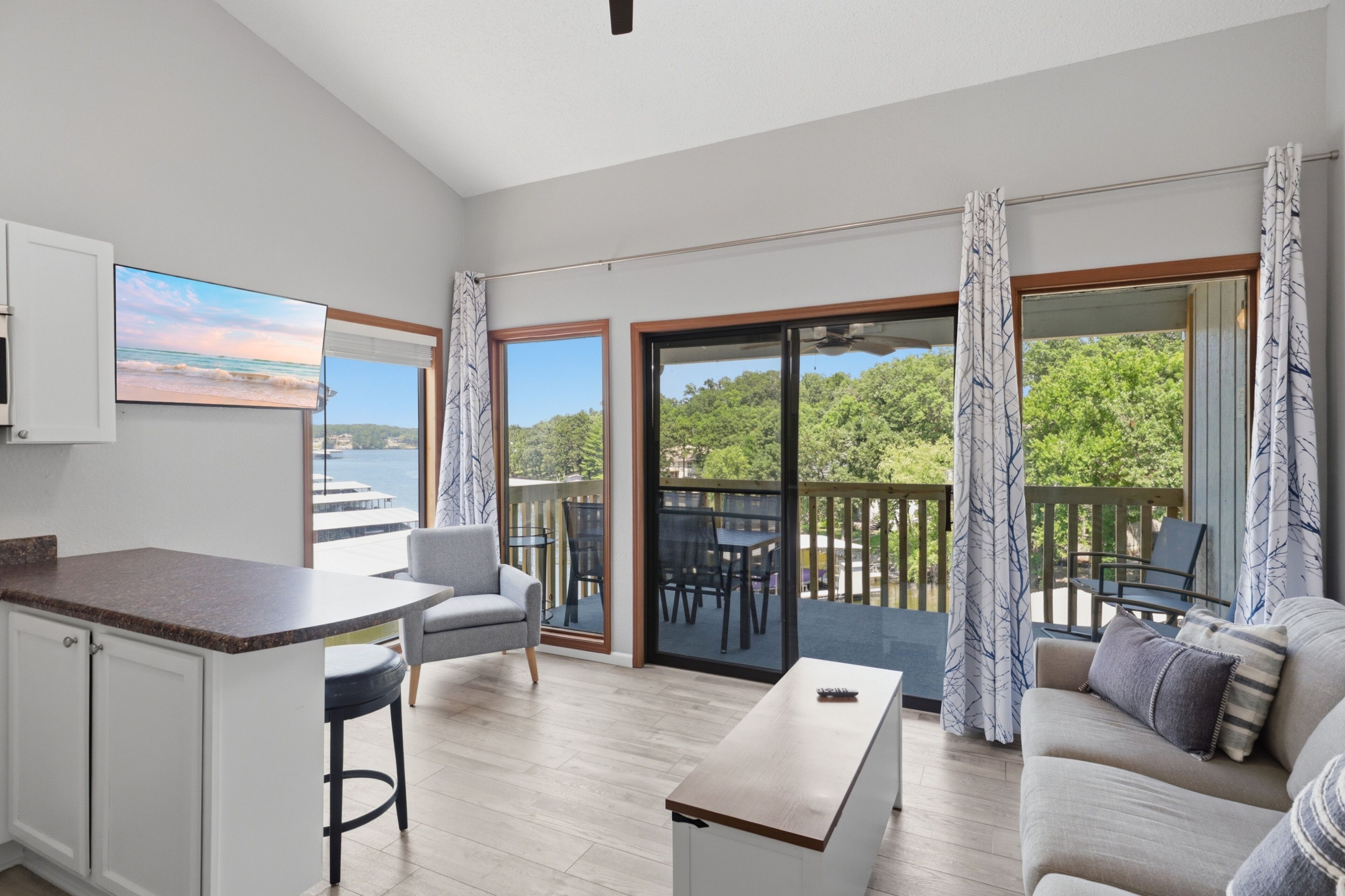Una sala de estar moderna con área de cocina, grandes puertas corredizas de vidrio que dan a un balcón y vista al mar.