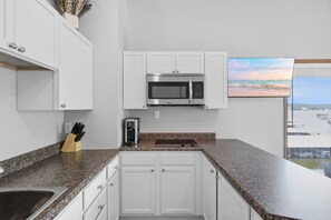 A modern kitchen with white cabinets, a stainless steel microwave, a coffee maker, and a view of the beach through a window. - H Lakefront Property, Remodeled, Boat Slip, Patio Views, Pool, Ideal Location! (Osage Beach)