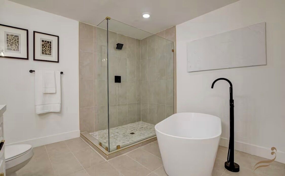 Een badkamer met een douche met glazen wand, een wit bad en een toilet.
