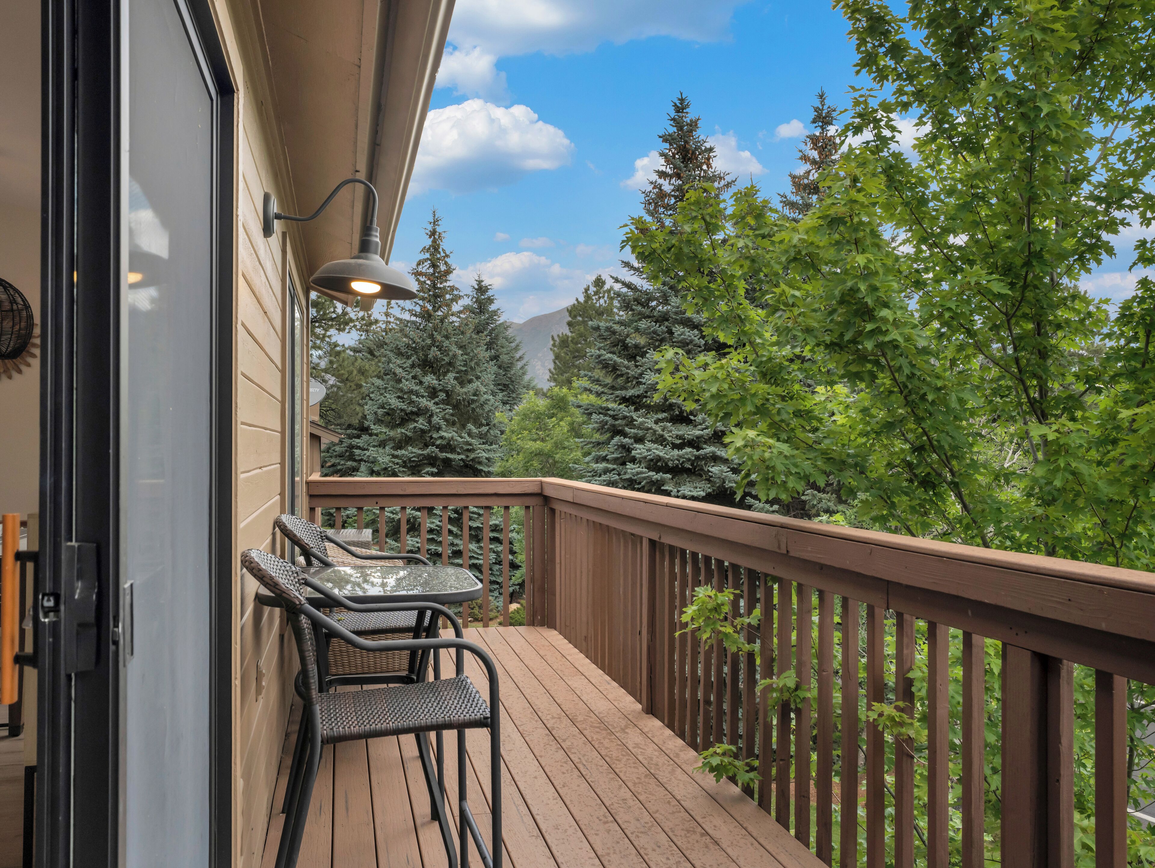 Une terrasse en bois avec une table et des chaises, une rambarde et une vue sur les arbres et les montagnes.