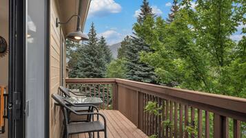 Une terrasse en bois avec une table et des chaises, une rambarde et une vue sur les arbres et les montagnes.