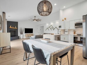 A modern kitchen with white cabinets, a stainless steel refrigerator, and a dining area with a table and chairs. - Cozy Mountain Condo @ Continental Golf Club (Flagstaff)