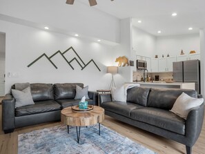 Ein modernes Wohnzimmer mit zwei Ledersofas, einem Holztisch und einer Küche im Hintergrund.