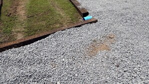 Un área de grava con un parche de césped y una tubería azul.