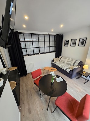 A modern living room with a sofa, a dining table, and a TV mounted on the wall.