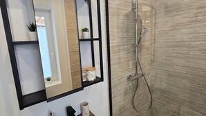 Un bagno moderno con uno specchio rettangolare, un mobile bagno in legno, un lavandino e una doccia con porta in vetro.