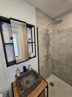 A modern bathroom with a rectangular mirror, a wooden vanity, a sink, and a shower with a glass door.