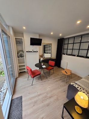 A modern room with a dining table, red chairs, a TV, a large window, and a small table with a lamp.