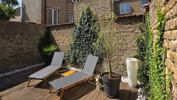 Una terrazza in legno con poltrone relax, una pianta in vaso e un muro in pietra.