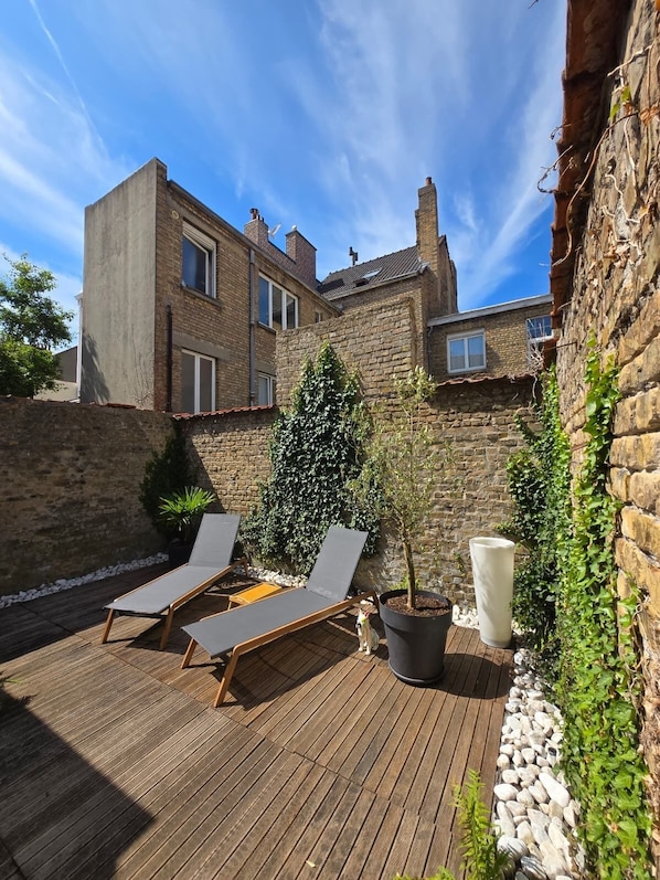 A wooden deck with lounge chairs, a potted plant, and a stone wall.