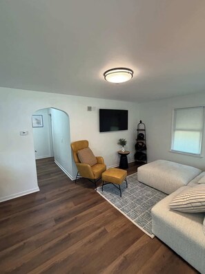 A modern living room with a sofa, a yellow armchair, a small side table, a flat-screen TV, and a ceiling light fixture. - 3 bedroom Updated Fully fenced yard (Rochester)