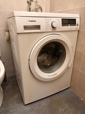 A white washing machine with a control panel, located in a bathroom with tiled walls and floor. - Nice apartment very close to the beach (Cubelles)