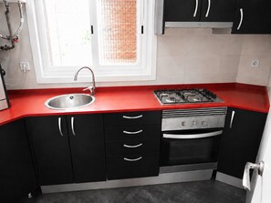 A modern kitchen with a red countertop, stainless steel sink, gas stove, and black cabinets. - Nice apartment very close to the beach (Cubelles)