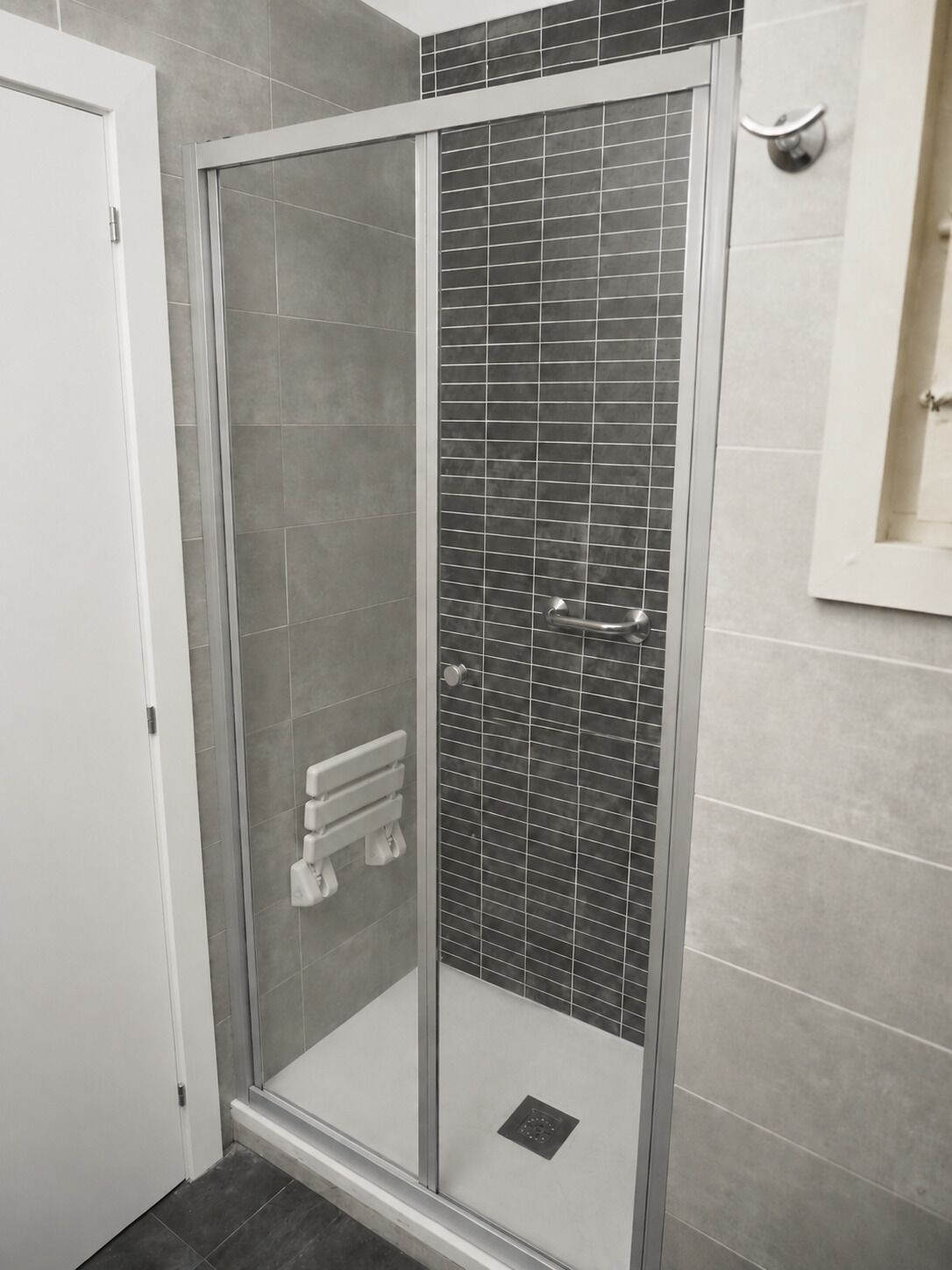 A shower with a glass door, tiled walls, and a white door.