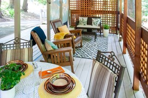 Un espacio al aire libre con techo, con sillas y una mesa, rodeado por una valla de madera celosíaca.