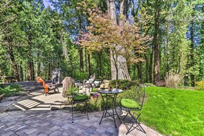 Un patio con mesa y sillas, rodeado por un jardín exuberante y altos árboles.