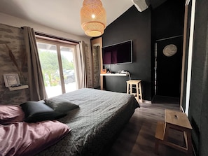 A bedroom with a bed, a desk, a television, and a window.