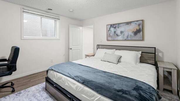 Een slaapkamer met een bed, een stoel, een nachtkastje, een deur en een raam met jaloezieën.
