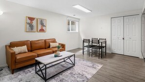 Een woonkamer met een bruine leren bank, een salontafel, een eettafel met stoelen en een witte deur.
