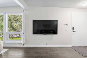 Ein Zimmer mit großem Fenster, einer Tür und einem an der Wand befestigten Fernseher.