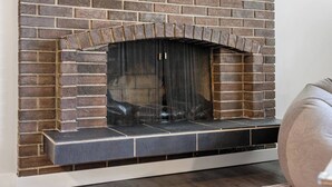 A brick fireplace with a metal screen, a white wall, and a dark floor. - 3 Bed | Min to UofC & Hospital | Garage (Calgary)