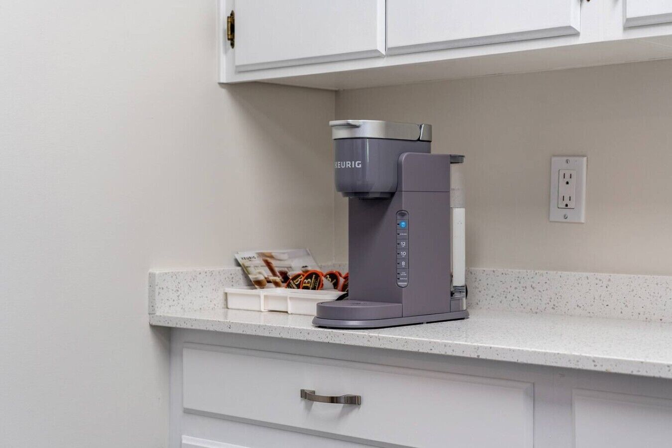 A coffee maker on a countertop with a coffee pod holder and a magazine.