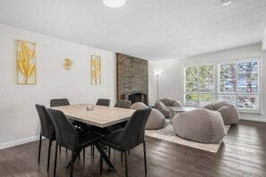 A modern interior with a dining table, chairs, bean bags, a brick wall, and large windows. - 3 Bed | Min to UofC & Hospital | Garage (Calgary)