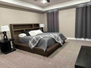 Ein Schlafzimmer mit einem Bett, zwei Nachttischen, einem Deckenventilator und einem Fenster mit Vorhängen.