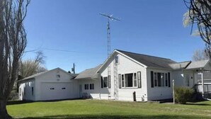 Ein zweistöckiges weißes Haus mit großem Vorgarten, einer Garage und einer hohen Antenne.