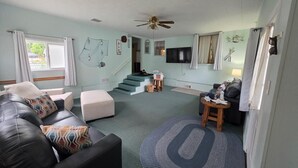 Ein Wohnzimmer mit einer Couch, einem Hocker und einem runden Teppich. Eine Treppe führt zu einer weiteren Ebene.